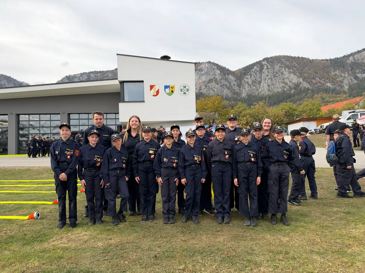 Eine Gruppe junger Menschen in Uniform steht vor einem Gebäude mit Bergen im Hintergrund.