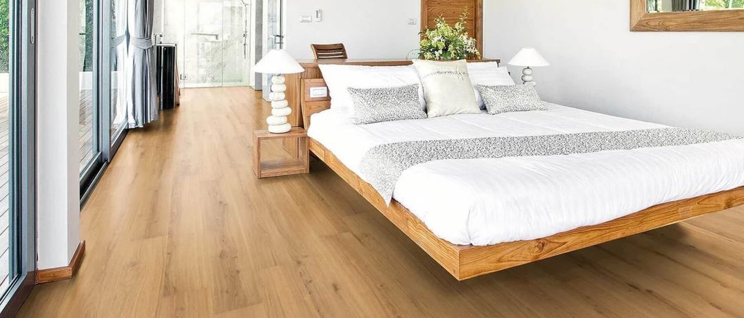 Ein modernes Schlafzimmer mit weißen Wänden, Holzböden und einem Bett mit Kissen. Zwei Lampen stehen auf beiden Seiten des Bettes. Ein hölzerner Schreibtisch befindet sich in der Ecke. Eine Glasdusche ist im Hintergrund zu sehen.