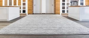 Ein leerer Raum mit einem großen grauen Teppich in der Mitte, hölzernen Schränken auf beiden Seiten und zwei weißen Türen.