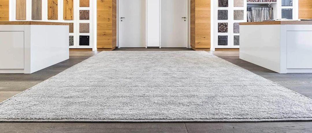 Ein leerer Raum mit einem großen grauen Teppich in der Mitte, hölzernen Schränken auf beiden Seiten und zwei weißen Türen.