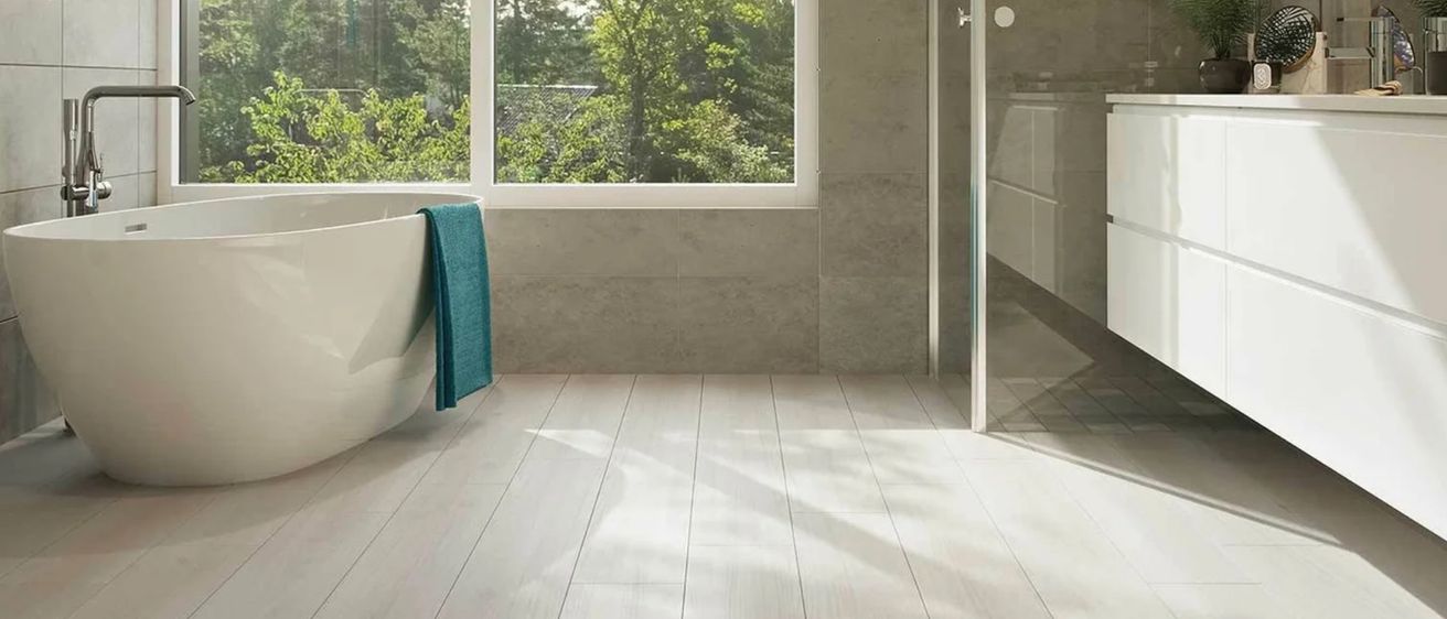 Ein Badezimmer mit einem großen Fenster und einer Badewanne. Ein grünes Handtuch hängt an der Wanne. Es gibt eine Dusche und eine Pflanze auf der Theke.