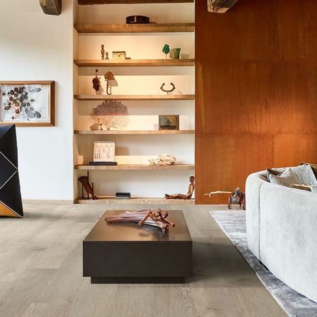 Ein modernes Wohnzimmer mit Holzboden, einem zentralen Tisch und einem weißen Sofa. Der Raum umfasst einen an der Wand montierten Rahmen, ein an der Wand montiertes Regal und eine Holzakzentwand.