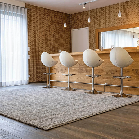 Eine Bar mit vier weißen Stühlen auf einem Teppich in einem Raum mit Holzboden und gemustertem Tapeten.