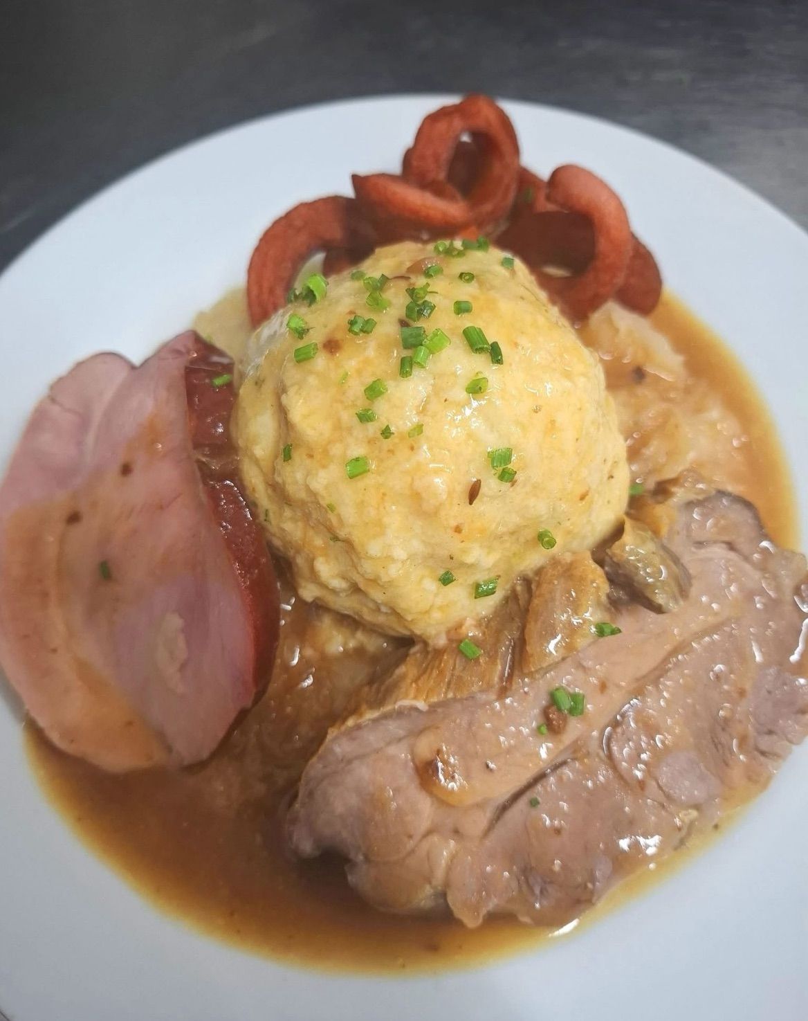 Ein Teller mit traditionellem deutschen Essen mit Fleisch, Knödeln und Soße, garniert mit Frühlingszwiebeln.