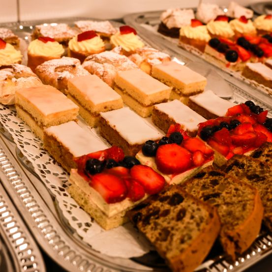 Ein Tablett mit Desserts bietet verschiedene Kuchen und Torten, einige mit Früchten wie Erdbeeren und Blaubeeren, andere mit weißer Glasur.