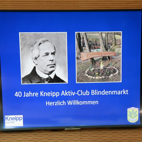 Ein blauer Bildschirm zeigt ein Foto eines Mannes und ein Schild mit der Aufschrift '40 Jahre Kneipp Aktiv-Club Blindenmarkt Herzlich Willkommen'. Das Foto des Mannes ist in Schwarz-Weiß.