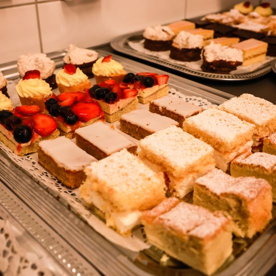 Eine Auswahl an Desserts, darunter Cupcakes und Kuchenstücke, ist auf Tabletts ausgestellt. Die Desserts variieren in Toppings und Dekorationen, wie Erdbeeren, Blaubeeren und Puderzucker.