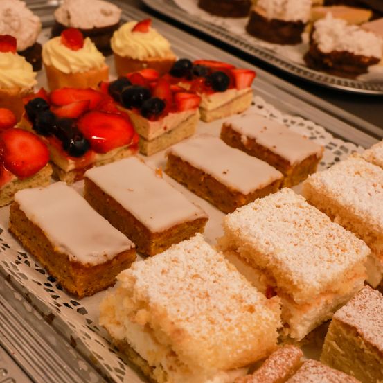 Ein Tablett mit Desserts, einschließlich Schichtkuchen mit Erdbeeren, Blaubeeren und Schlagsahne und Kuchenquadrate mit weißer Glasur und Puderzucker.