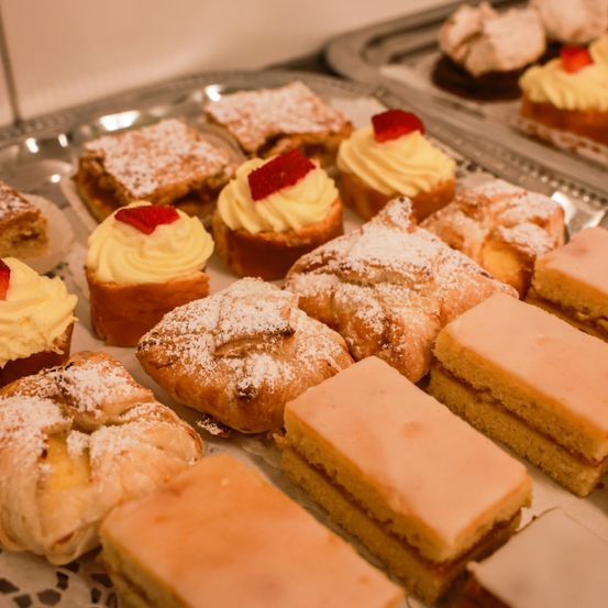 Ein Tablett mit verschiedenen Desserts, darunter ein Stück mit gelber Glasur und roten Früchten, ein quadratisches Gebäck und andere mit Puderzucker.