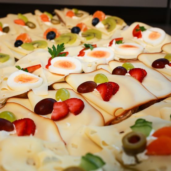 Nahaufnahme einer Auswahl an Käsescheiben, garniert mit gekochten Eiern, Erdbeeren, Trauben, Oliven und grünen Paprika.
