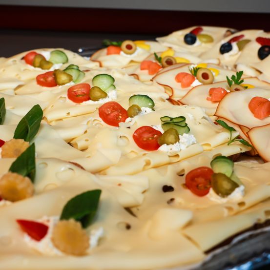 Eine Nahaufnahme einer Käseplatte mit verschiedenen Toppings wie Tomaten, Gurken, Oliven und Kräutern auf einem silbernen Tablett.