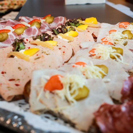 Eine Auswahl an Sandwiches und Fleisch, garniert mit Käse, Gurken und Gemüse, wird auf einem Tisch präsentiert.