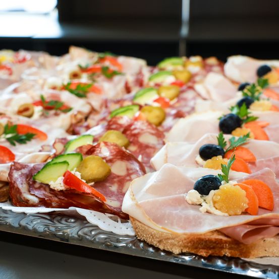 Eine Nahaufnahme verschiedener Sandwiches und Charcuterie, einschließlich Scheiben von Schinken, Salami und Gemüse, auf einem silbernen Tablett angeordnet.