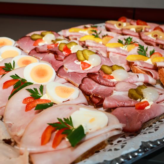 Eine Platte mit verschiedenen Fleischscheiben, Eiern und Gemüse. Jedes Stück ist mit Petersilie, Gewürzgurken und Käse garniert. Die Eier sind geschnitten und auf dem Fleisch platziert.
