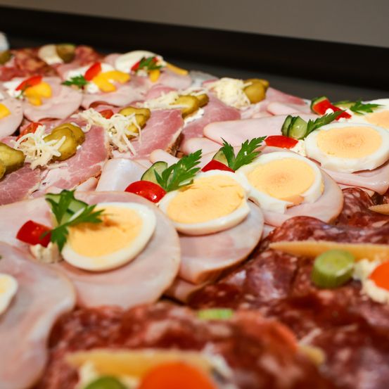 Ein Tablett mit verschiedenen Fleischsorten und Eiern, garniert mit Kräutern, Käse, Gurken und Tomaten, serviert auf einem dunklen Hintergrund.