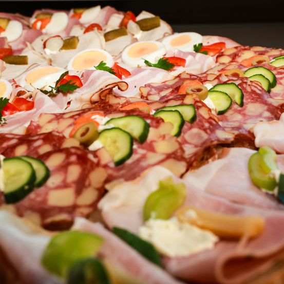 Eine Nahaufnahme einer Charcuterie-Platte mit verschiedenen Fleischsorten, Käse und Gemüse. Das Angebot umfasst geschnittene Salami, gekochte Eier, Gurken und Oliven.