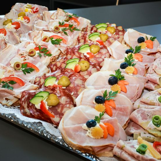 Eine Auswahl an Fleischscheiben, verziert mit Oliven, Gurken, Karotten und Petersilie auf einem silbernen Tablett. Die Fleischsorten umfassen Salami, Prosciutto und andere Wurstwaren.
