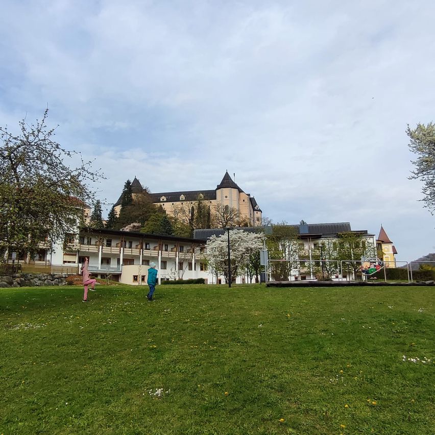 Zwei Personen spielen auf einem Rasen vor einem großen Schloss unter einem bewölkten Himmel.