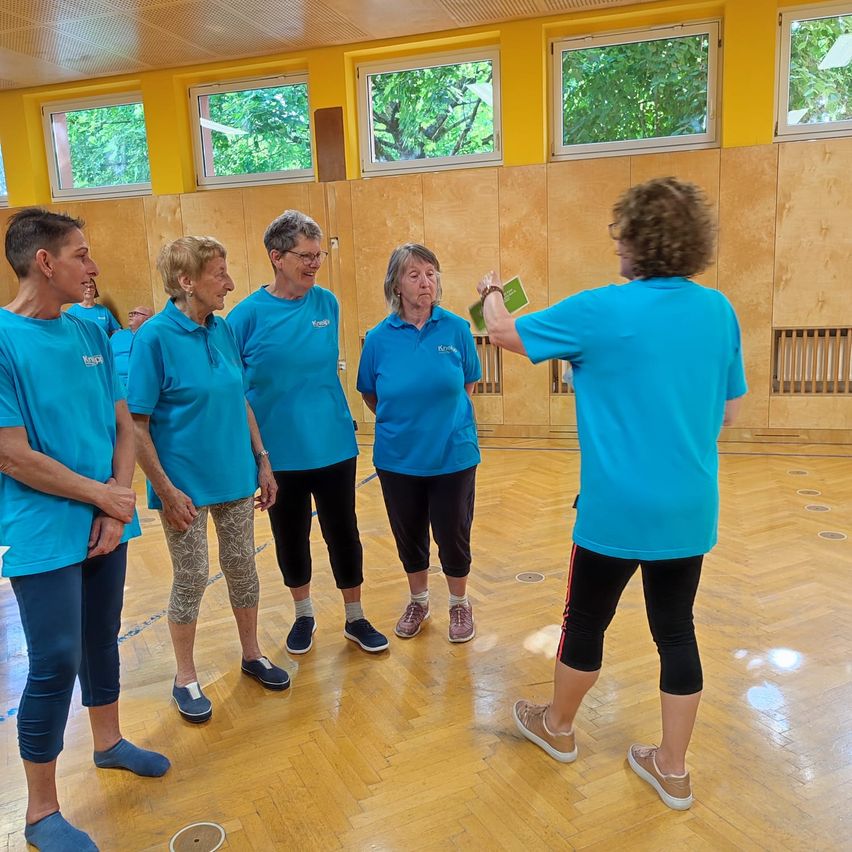 A group of women wearing blue shirts are standing in a gym. One woman holds a green card.