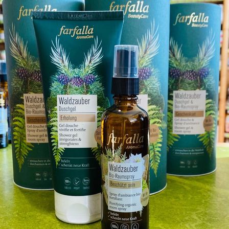 Mehrere Flaschen des farfalla Waldzauber Bio-Raumsprays auf einem Tisch, mit Kiefernzapfen und Blättern. Die Flaschen umfassen ein Duschgel und Spray sowie einen Raumspray.