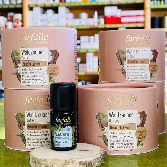 Eine Sammlung von Waldzauber-Diffusoren und ätherischen Ölen von farfalla AromaCare auf einem Ladentisch. Die Diffusoren sind zylindrisch und haben ein Etikett, das 'Waldzauber Duftset' liest. Die Öle sind in kleinen schwarzen Flaschen.