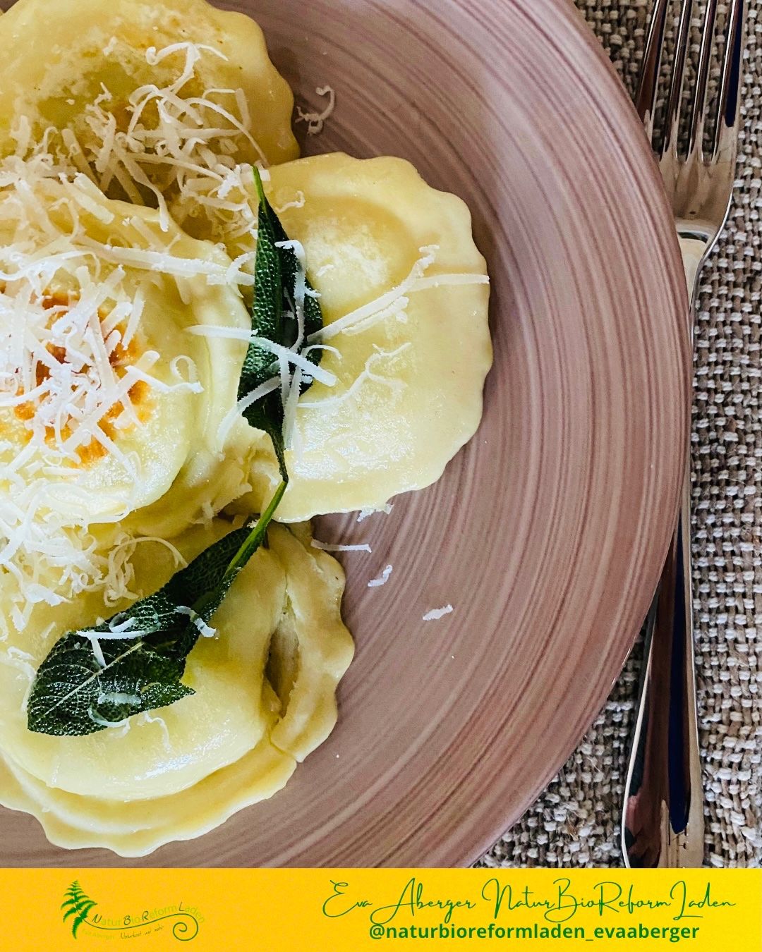 Ein Teller mit Ravioli, garniert mit geriebenem Käse und Salbeiblättern, auf einer strukturierten Oberfläche.