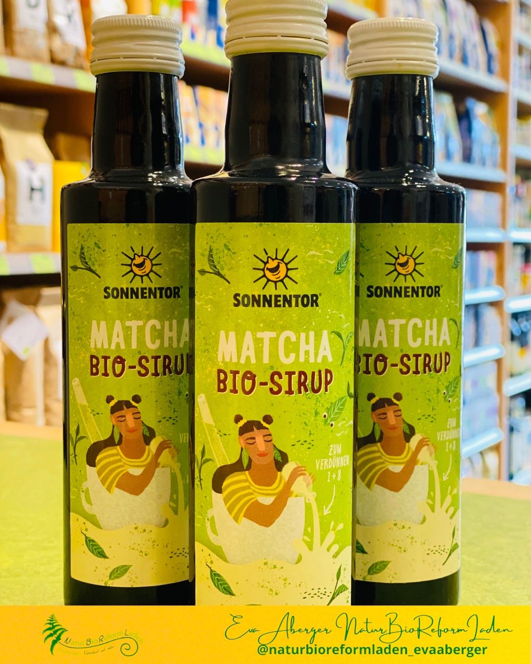 Drei Flaschen Sonnentor Matcha Bio-Sirup stehen in einem Geschäft auf einem Tresen. Jede Flasche zeigt eine Frau in einer Tasse mit Blättern.