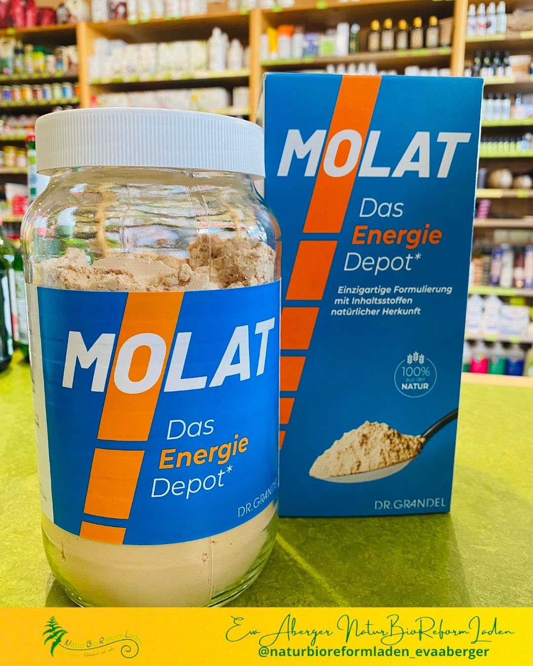 Ein Glas des Molat Das Energie Depot Nahrungsergänzungsmittels neben seiner Packung. Das Glas ist mit weißem Pulver gefüllt, und die Packung ist blau mit orange-weißen Streifen.
