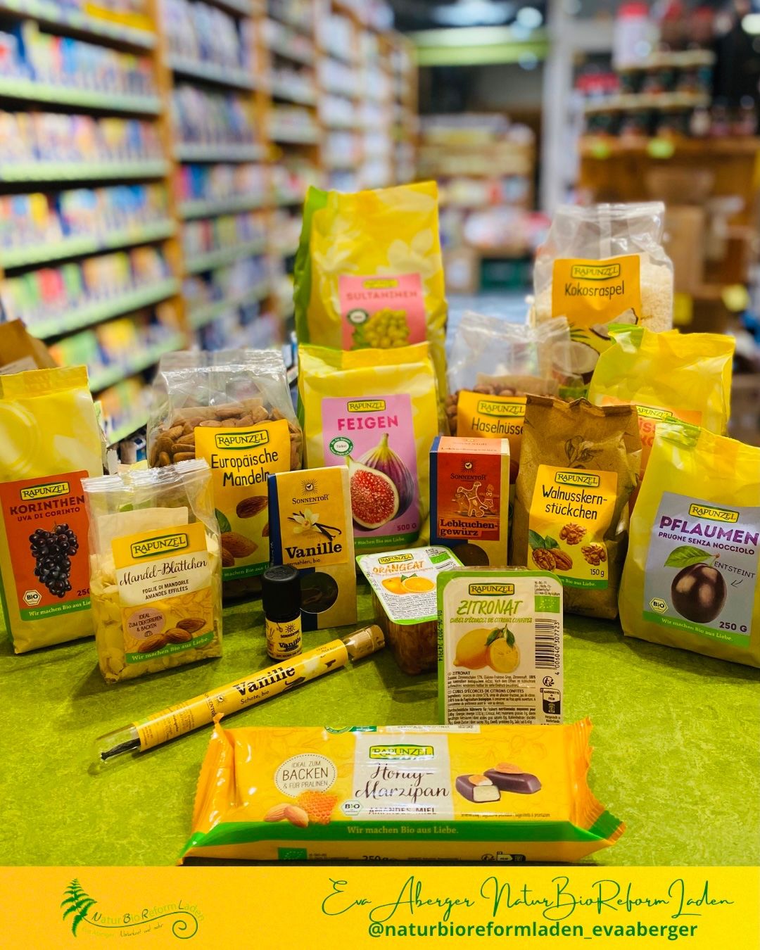 Ein Tisch voller verschiedener Snacks und Süßigkeiten in gelber und grüner Verpackung, einschließlich Mandel-, Zitronen- und Marzipan-Geschmack, präsentiert in einem Geschäft mit Regalen im Hintergrund.