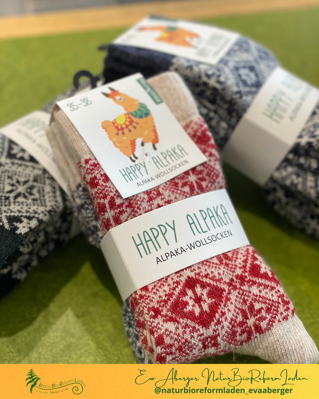 Ein Paar rot-weiß gemusterte Socken mit einem Alpaka auf dem Etikett. Das Etikett lautet 'Happy Alpaka Alpaka-WolleSocken'.