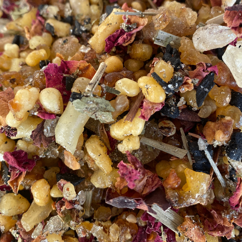 Eine Nahaufnahme einer Mischung aus Kräutern, Gewürzen und getrockneten Blumen. Sie enthält unterschiedliche farbige Blütenblätter, gelbe Samen und kleine Pflanzenstiele. Die Zutaten scheinen für kulinarische oder medizinische Zwecke vorbereitet zu sein.