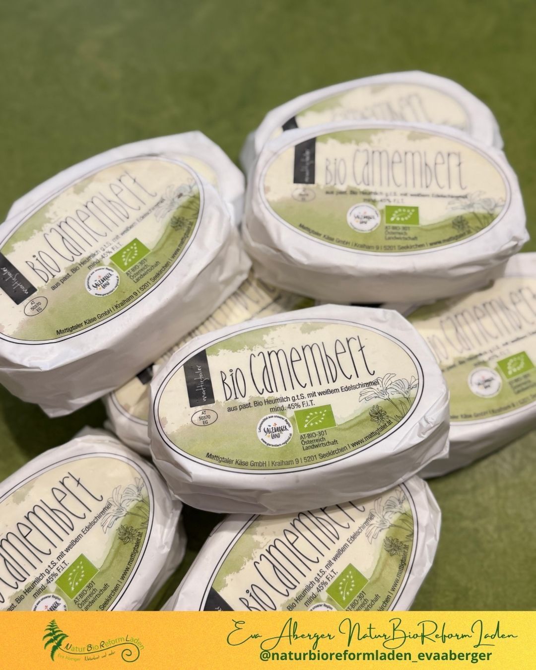 Ein Stapel Bio-Camembert in weißer Verpackung mit grünen Etiketten. Die Etiketten enthalten Details wie pasteuriert, biologisch und umweltfreundlich.