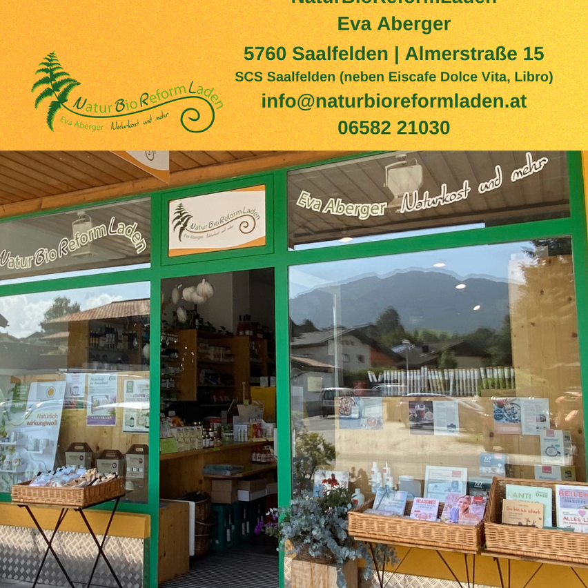 A storefront with a green door and window displays, showcasing various products and promotional materials. The shop is named Eva Aberger and is located in Saalfelden.