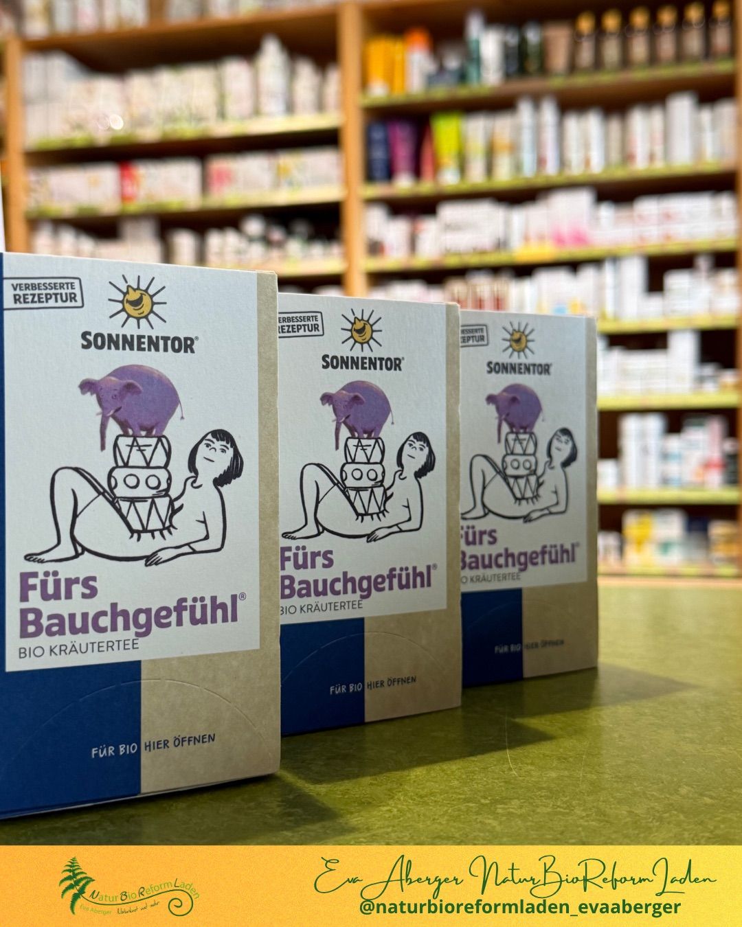 Drei Schachteln von Sonnentors Bio-Kräutertee mit der Aufschrift 'Fürs Bauchgefühl' sind auf einem Tisch in einem Geschäft ausgestellt, mit Regalen voller Produkte im Hintergrund.