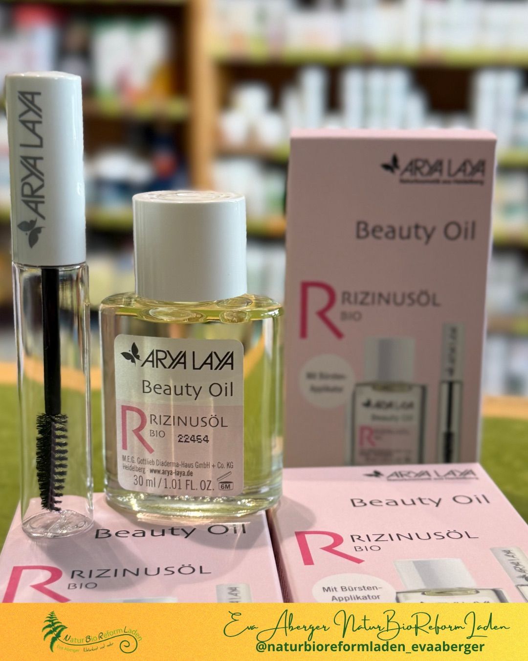 Eine Nahaufnahme einer Flasche Arya Laya Bio Rizinusöl Beauty Oil mit einem Mascara-Wimpern und einer rosa Box auf einer grünen Oberfläche.