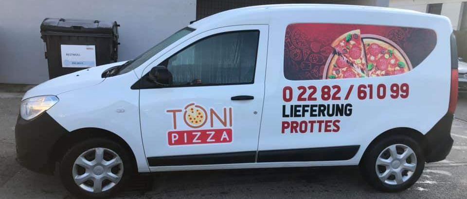 Ein weißer Lieferwagen mit der Aufschrift 'TONI PIZZA' und '0 22 82 / 610 99' steht vor einem Gebäude. Daneben befindet sich ein Mülleimer.