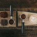 Zwei Kaffee-Utensilien, Kaffeebohnen und ein Latte mit Herzdesign auf einer hölzernen Oberfläche.