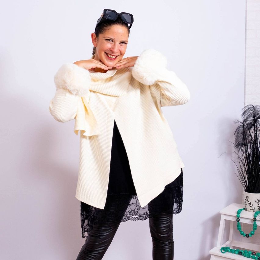 A woman in black leather pants and a white fur-trimmed cardigan is posing for a photo in a white room.