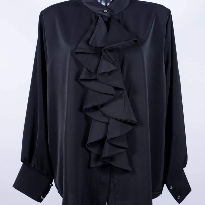 Eine schwarze Bluse mit langen Ärmeln und einem gerüschten Kragen, ausgestellt auf einem Mannequin.