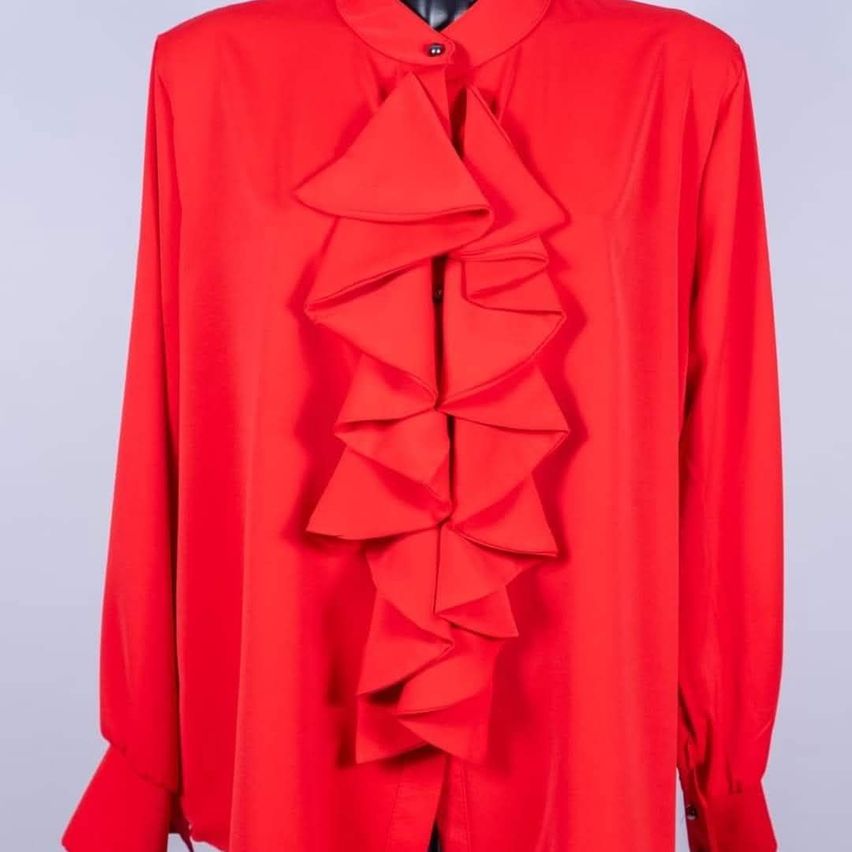 Ein hellrotes Langarm-Blusenhemd mit Rüschen am Kragen, ausgestellt auf einem Mannequin.