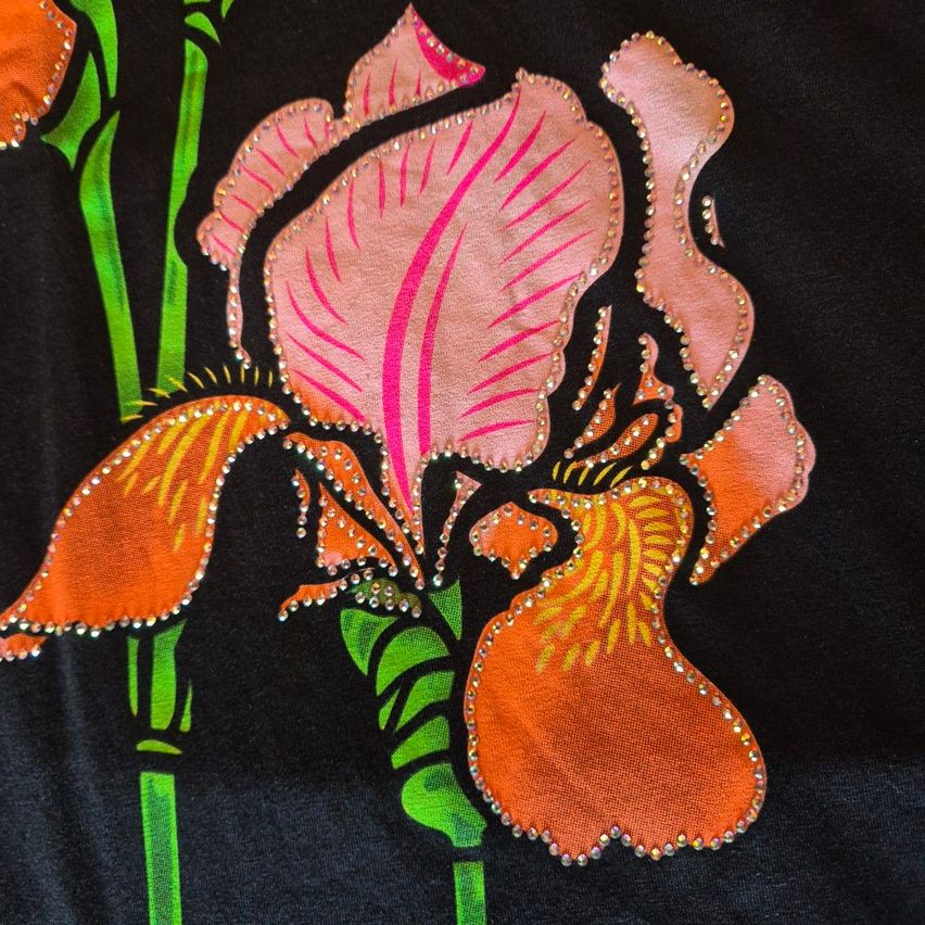 Eine Nahaufnahme einer handbestickten Irisblüte mit rosa Blütenblättern und orangefarbenen Staubblättern auf schwarzem Hintergrund. Die Blütenblätter sind mit Perlen verziert.