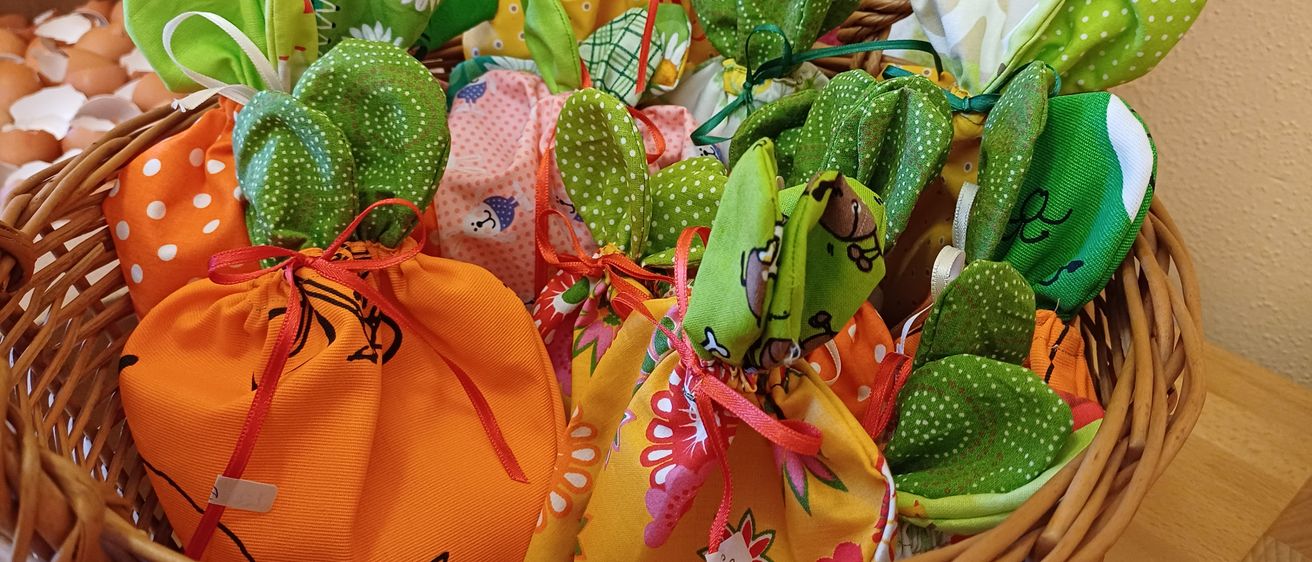 Ein Korb aus Weide gefüllt mit bunten Stoffsäckchen mit Blumenmustern, mit Bändern gebunden. Einige haben Blumenmuster, andere haben grüne Blätter und Punkte.