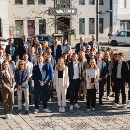 Eine Gruppe von Fachleuten in Geschäftskleidung posiert für ein Foto vor einem modernen Gebäude mit einem Schild, das 'Parkasse' besagt.