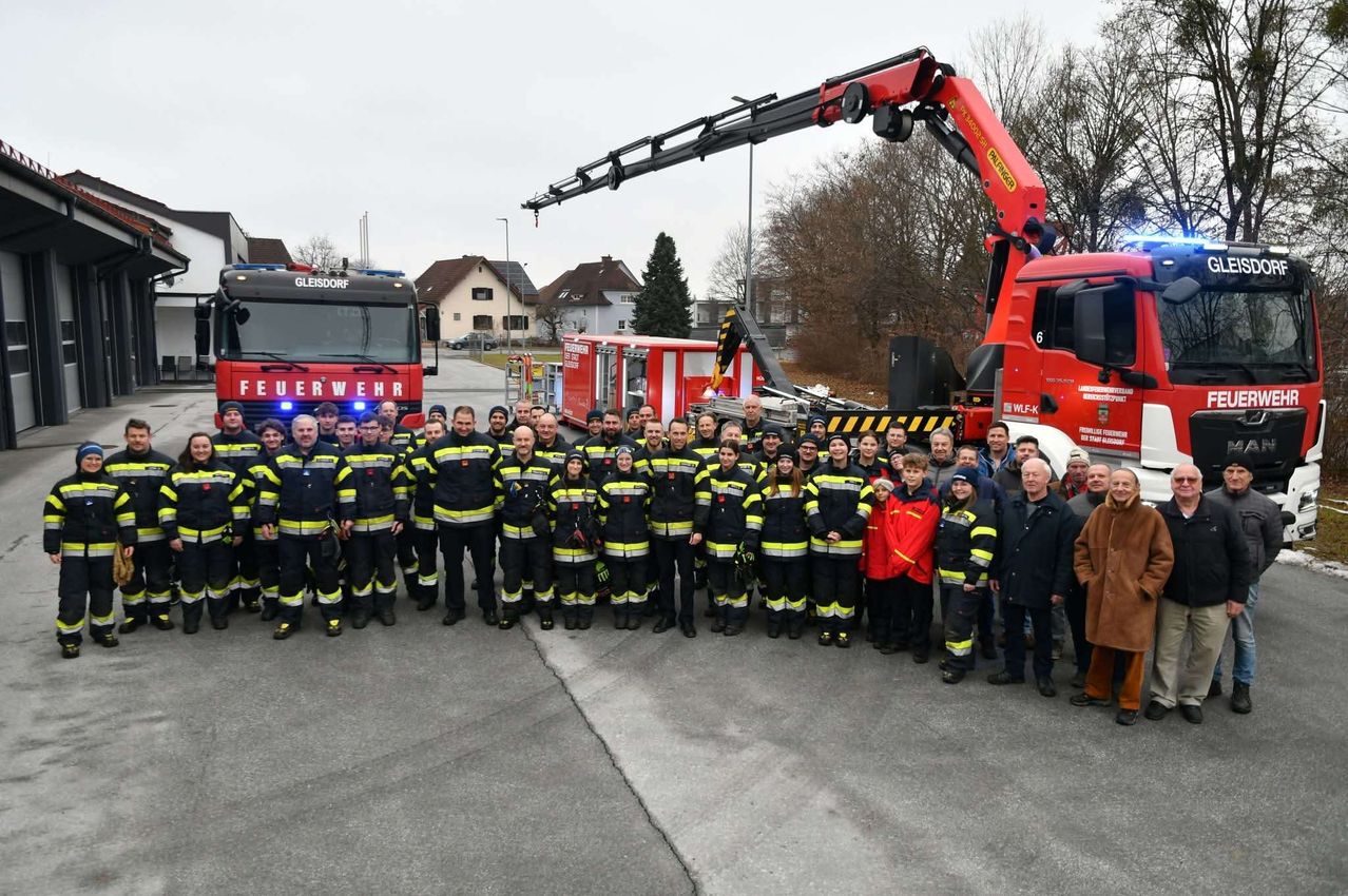 Eine Gruppe von Feuerwehrleuten posiert für ein Foto vor zwei Feuerwehrwagen, von denen einer einen Kran auf dem Dach hat.