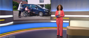 Eine Frau im Rollstuhl wird von einer älteren Frau vor einem blauen Auto unterstützt. Eine erwachsene Frau steht in der Nähe.