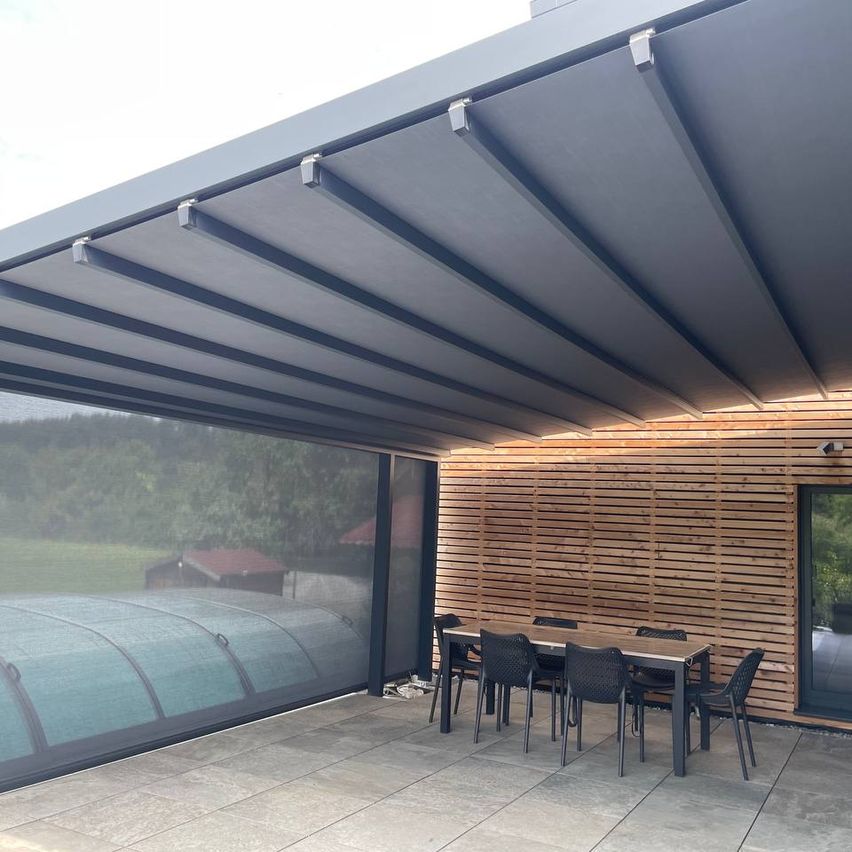 Ein Outdoor-Terrassenbereich mit ausziehbarem Dach, Holzwänden und einem Esstisch. Die Terrasse hat ein modernes Design mit einem grauen Dach und schwarzen Stühlen.