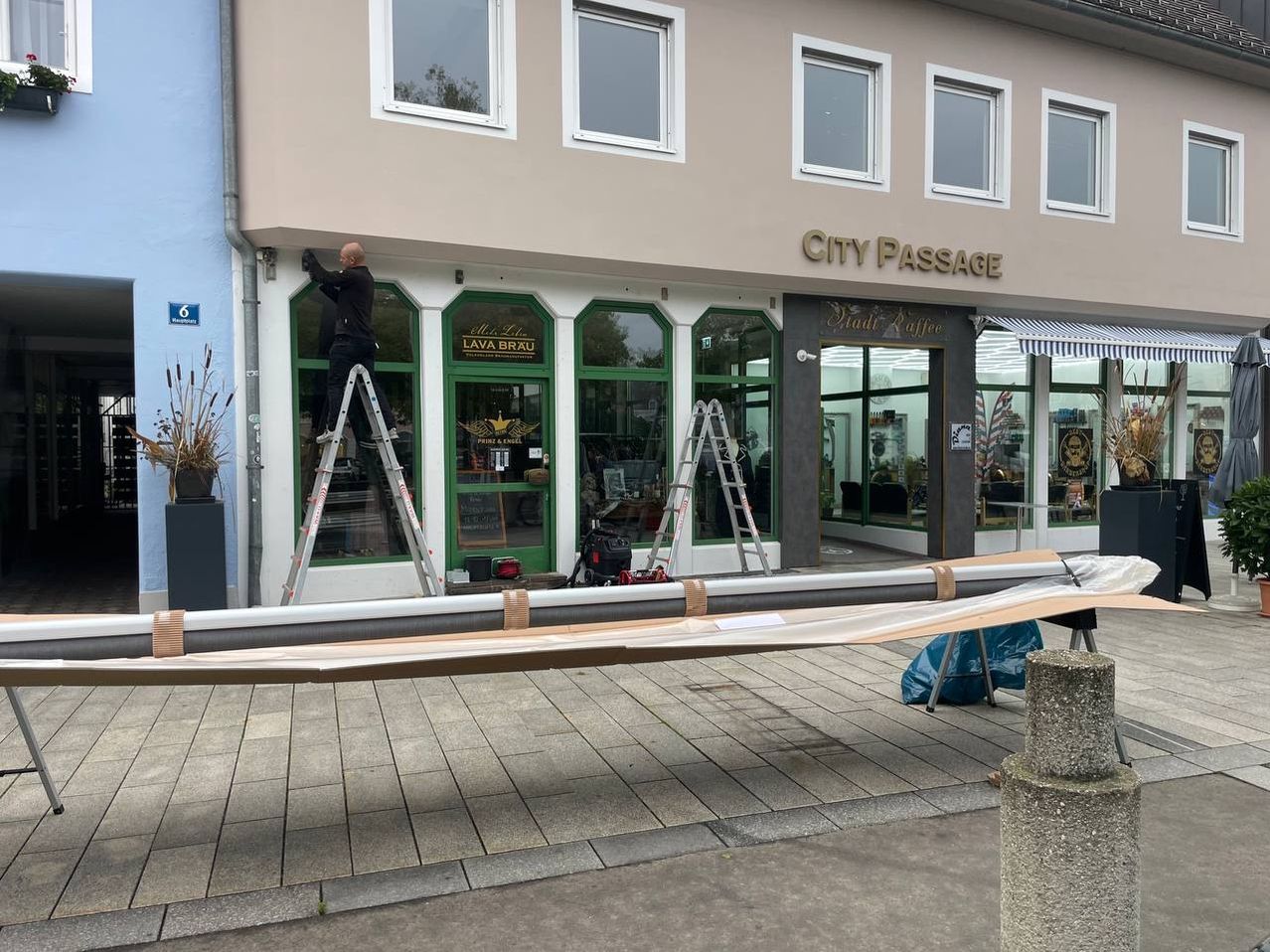 Ein Mann arbeitet an einem Fenster eines Gebäudes namens City Passage. Er steht auf einer Leiter. Eine Leiter ist neben dem Fenster aufgestellt.
