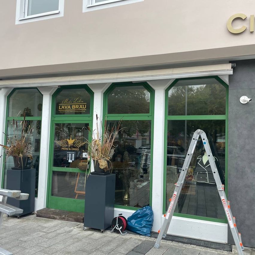 Vor einem Gebäude mit dem Schild Lava Brau stehen Pflanzen in Pflanzgefäßen, eine Leiter und ein Beutel auf dem Bürgersteig.