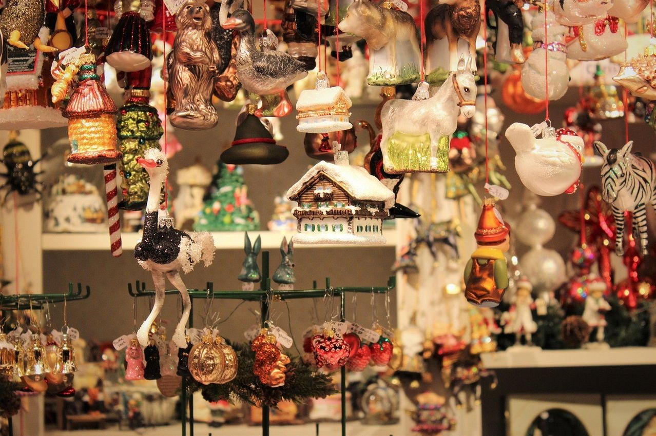 Eine Ausstellung farbenfroher Glasornamente hängt an einem grünen Metallständer. Die Designs umfassen Tiere, ein Haus und Früchte.