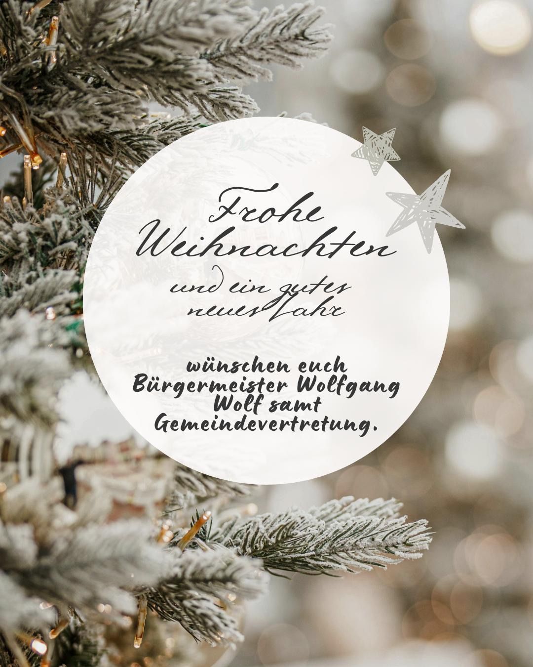 Ein weißer kreisförmiger Ornament mit Sternendesign hängt an einem Weihnachtsbaum. Es enthält eine Botschaft auf Deutsch, die 'Frohe Weihnachten und ein gutes neues Jahr' lautet und eine Unterschrift von 'Bürgermeister Wolfgang Wolf' enthält.